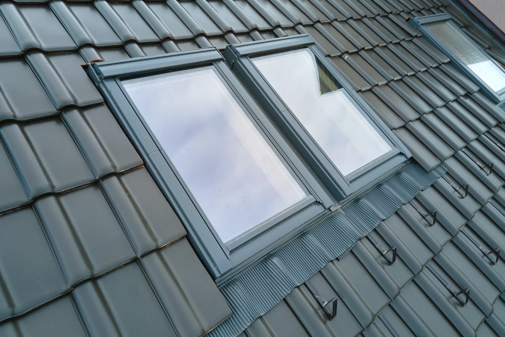 Closeup of attic window on house roof top covered with ceramic shingles. Tiled covering of building